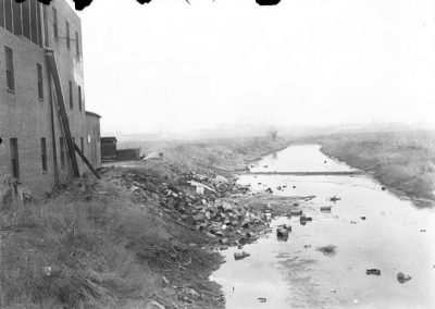 black and white photograph of building, trash, and waterway