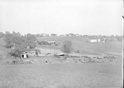 black and white photograph of farm buildings and houses in distance