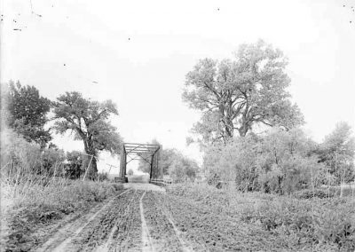 black and white photo of a bridge covered with a tressle along a dirt road with trees and vegetation on both sides