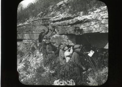 Black and white photograph of rock ledge with several men looking at the rock