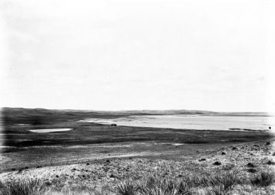 black and white photo of portion of lake with sandy, grassy landscape shoreline
