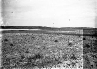 black and white photo of lake in far distance with grass and sandy land in foreground