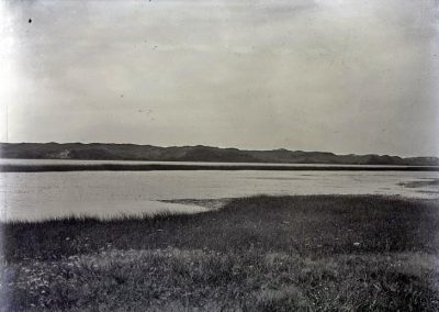 black and white photo of lake with grass shore in foreground and bluffs in the distance