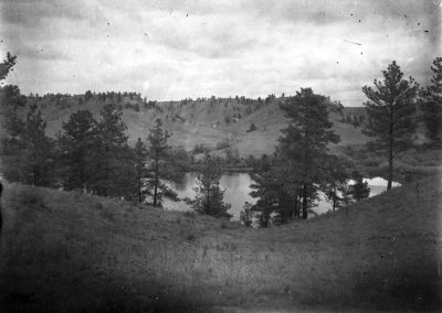 black and white photo of pond amid bluffs with evergreen trees along shore