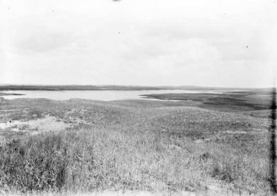 black and white photo of lake in distance with grass slopes in foreground