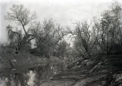 black and white photo of creek with large area of embankment and trees showing along side