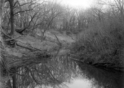 black and white photo of creek and banks with trees