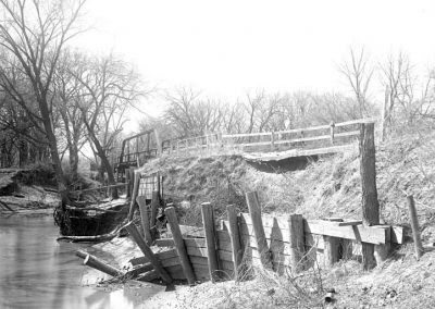 black and white photo of damage boards along a creek and bridge