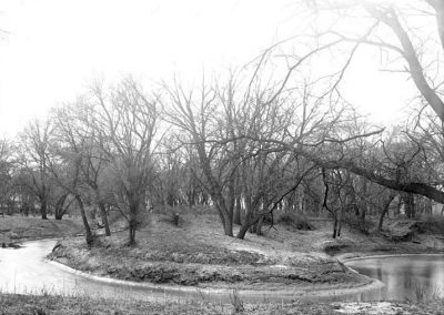 black and white photo of creek along a bend and trees on banks